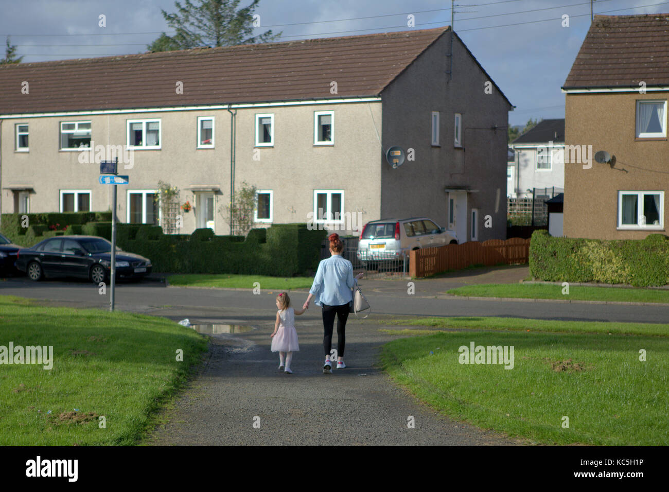 Madre e figlia sul percorso nella zona suburbana di sistema di alloggiamento progetto camminare tenendo le mani sulla strada linnvale Clydebank, Regno Unito Foto Stock