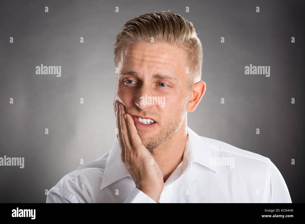 Giovane uomo che soffre di mal di denti contro uno sfondo grigio Foto Stock