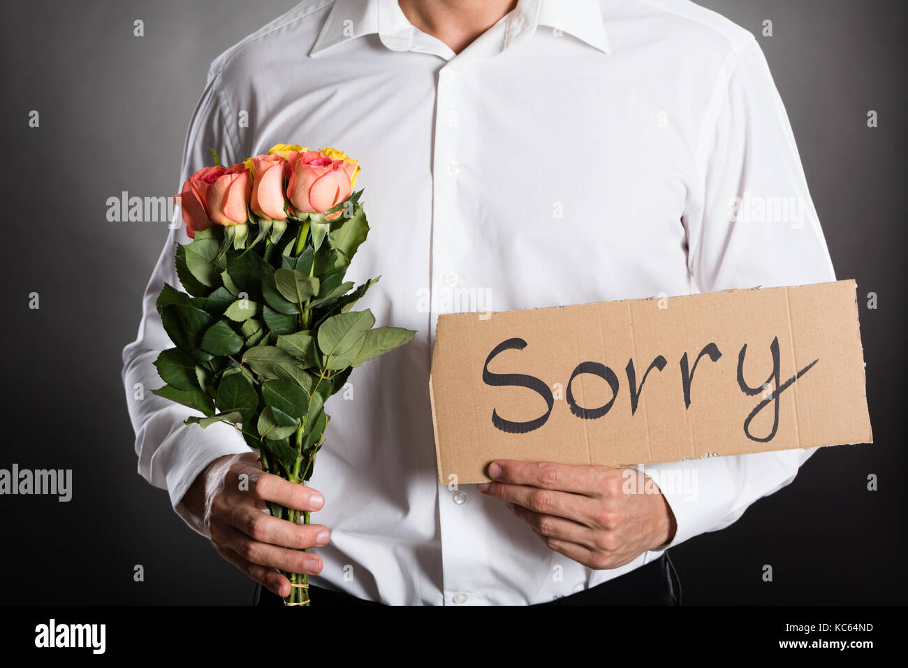 Uomo con le rose e il testo spiacenti scritto sul cartone contro uno sfondo grigio Foto Stock