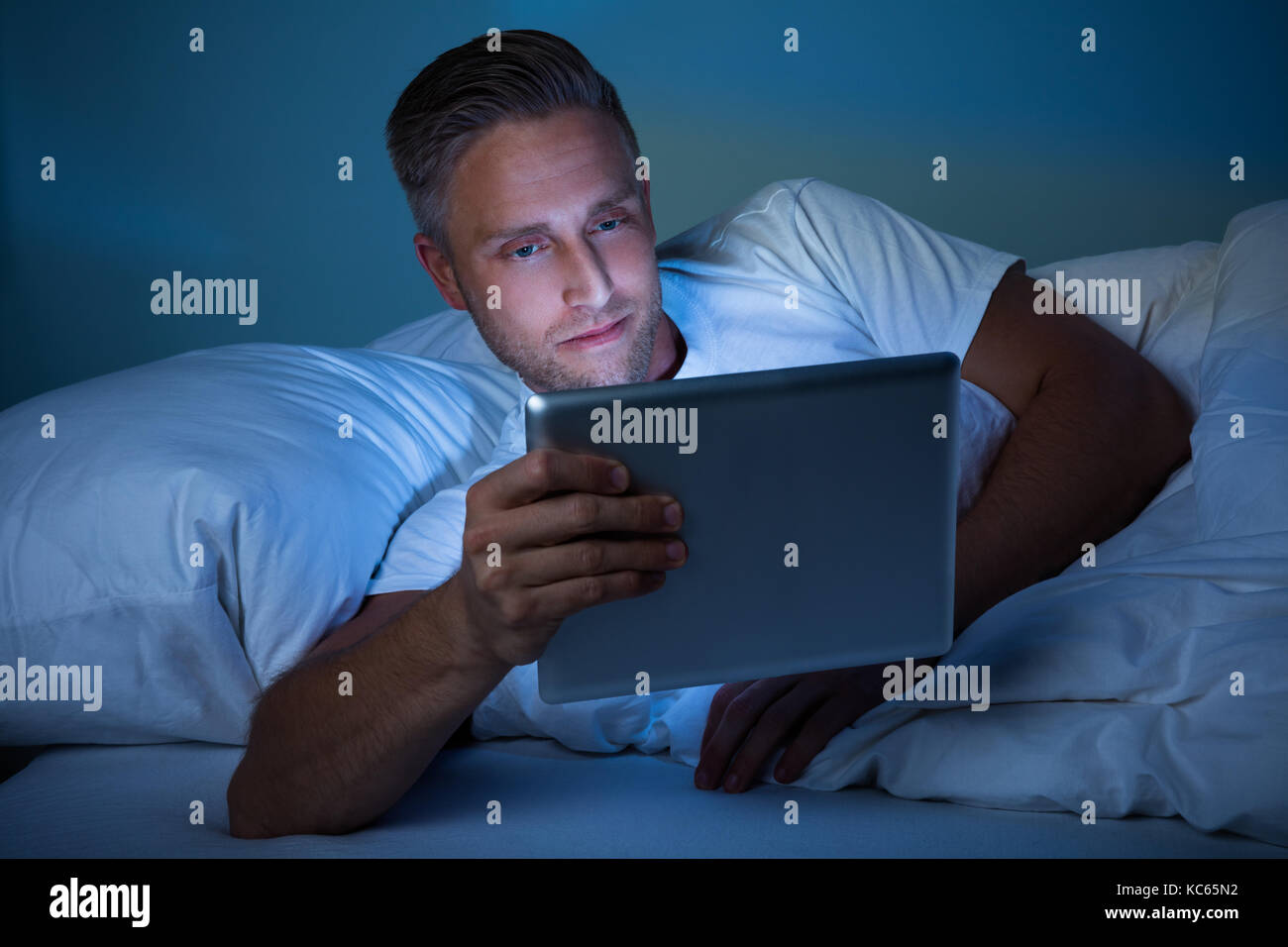 Uomo disteso sul letto guardando illuminato tavoletta digitale Foto Stock