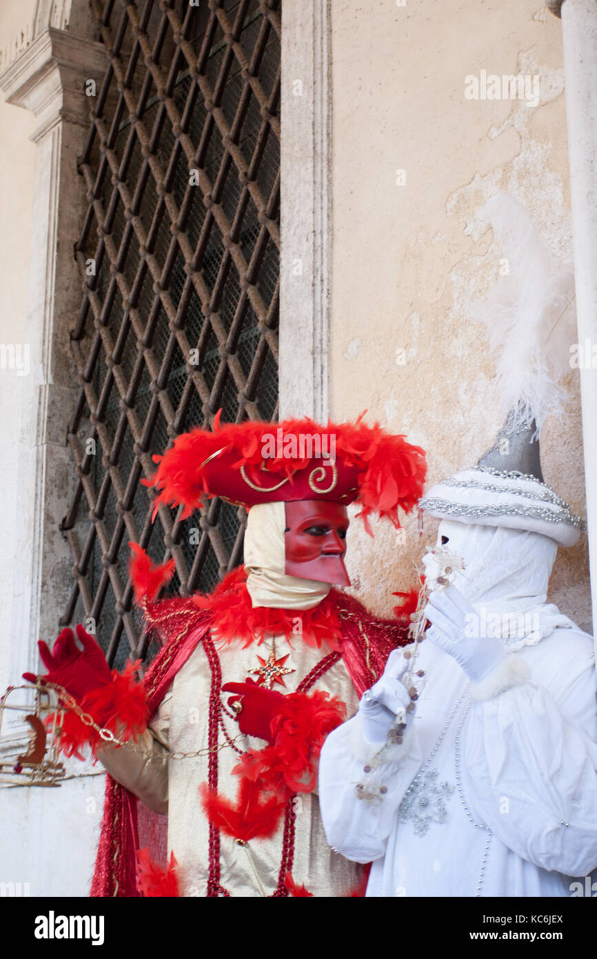 Maschera rossa di casanova parlando con colombina, al carnevale di Venezia, Italia. sfondo composto da una vecchia finestra con reticolo di ferro. Foto Stock