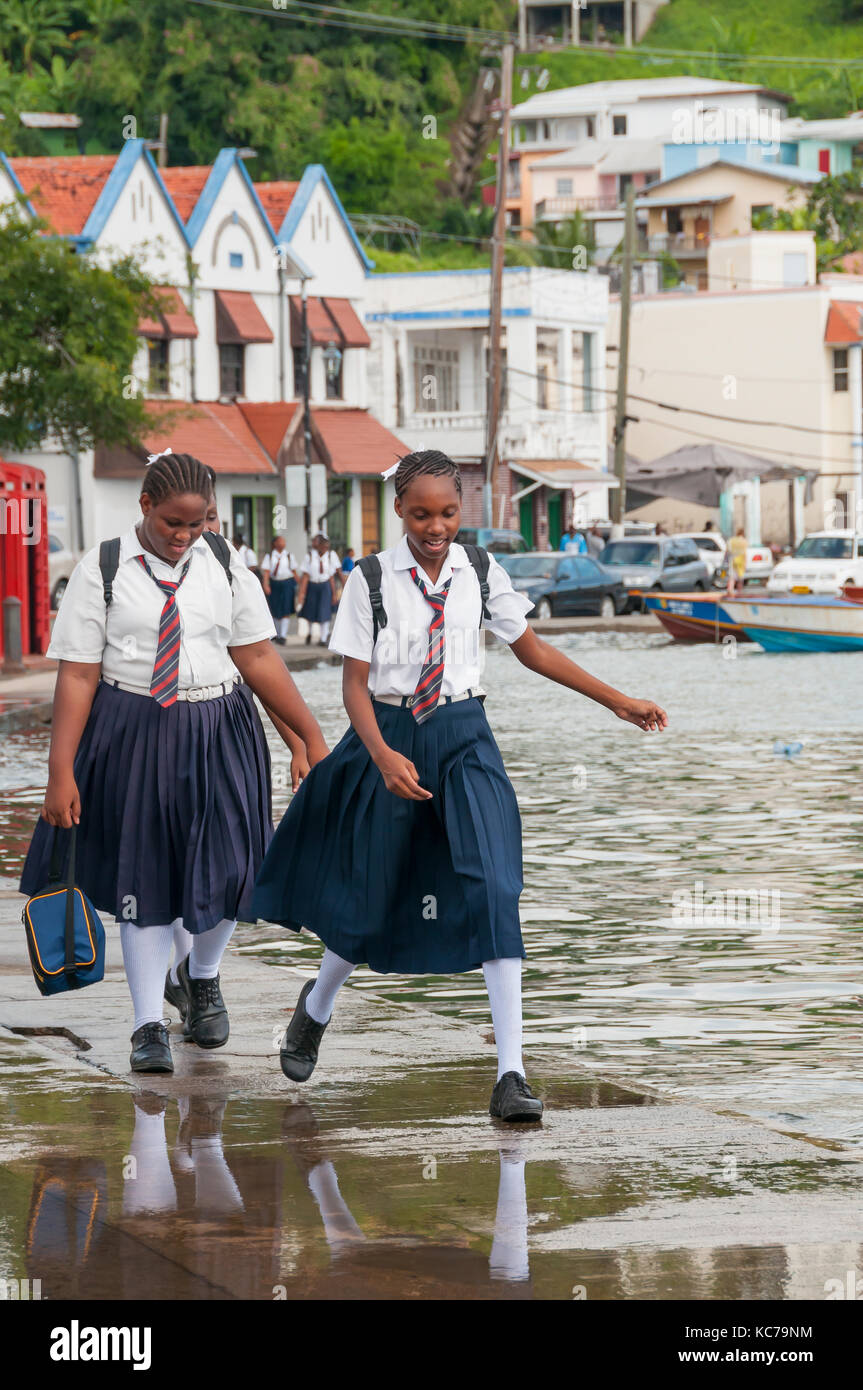 Due ragazze della scuola in divisa con cravatte jump pioggia pozzanghera a St George Carenage Grenada Foto Stock
