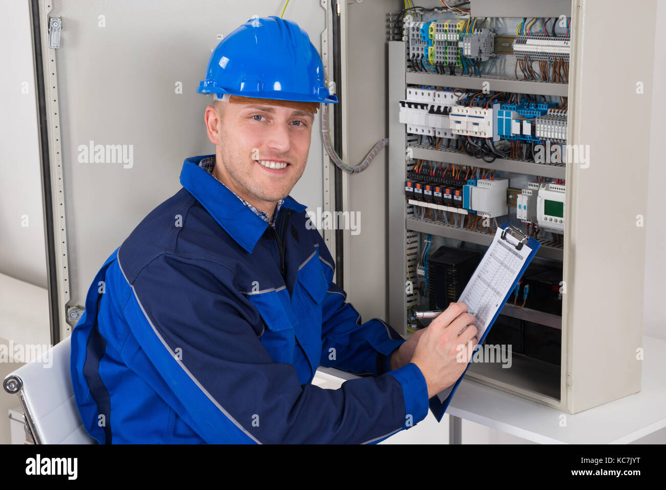 Giovane maschio tecnico azienda clipboard mentre esaminando scatola fusibili Foto Stock
