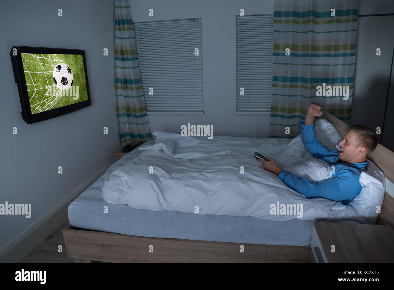Giovane uomo guardando la partita di calcio in televisione nella sua camera da letto Foto Stock