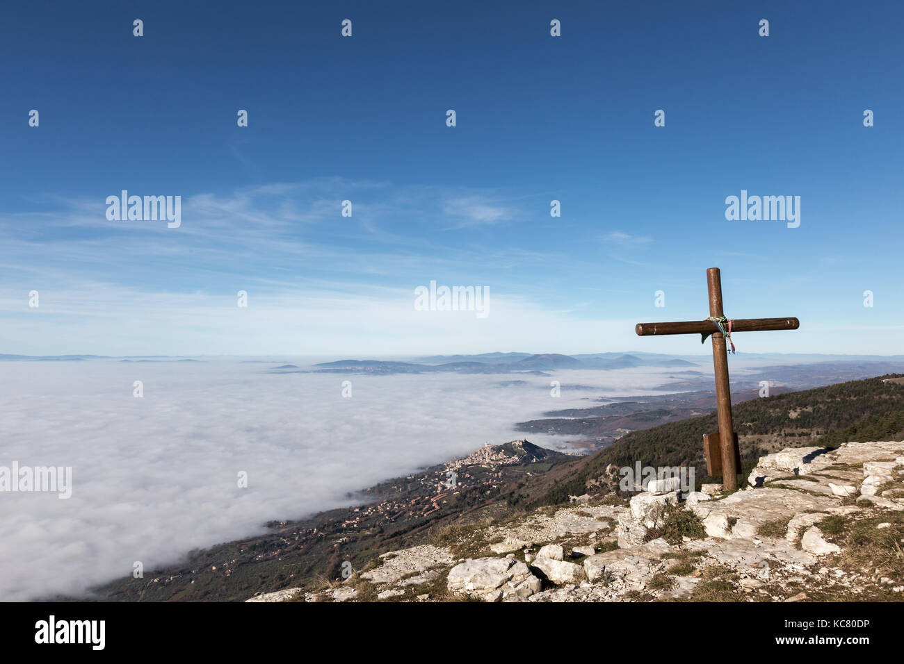 Una croce di legno in cima del monte Subasio, con un mare di nebbia al di sotto e la città di Assisi (Umbria) in background Foto Stock