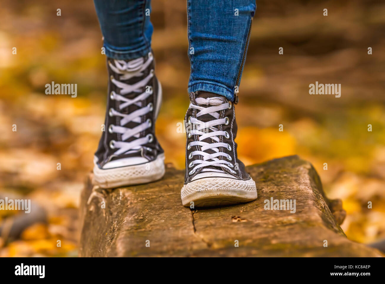 Ragazza indossa con nero sneakers camminando sul legno più cadono le foglie in autunno. Foto Stock