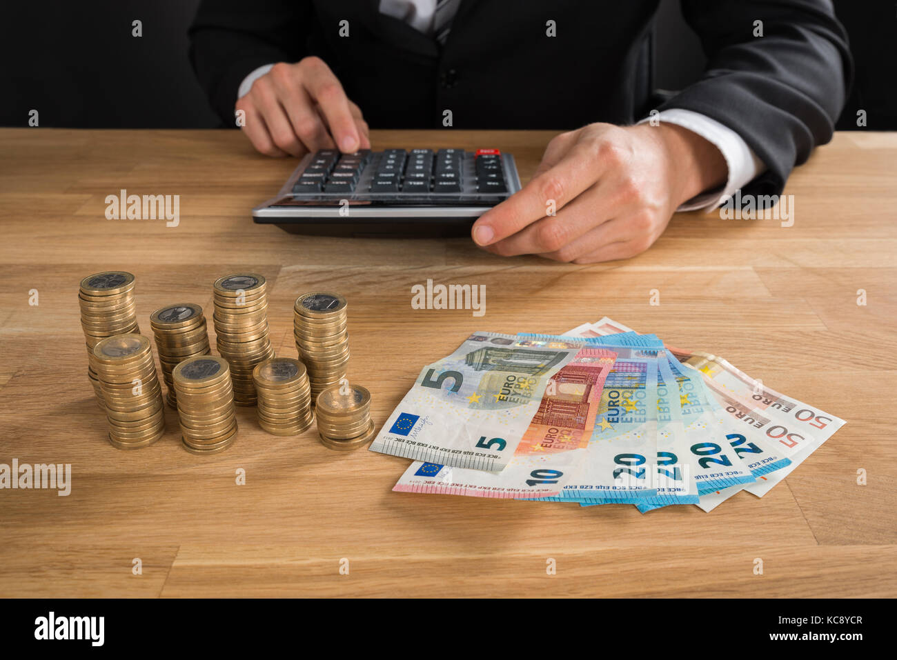 Close-up del giovane imprenditore utilizzando la calcolatrice con monete e banconote sulla scrivania Foto Stock
