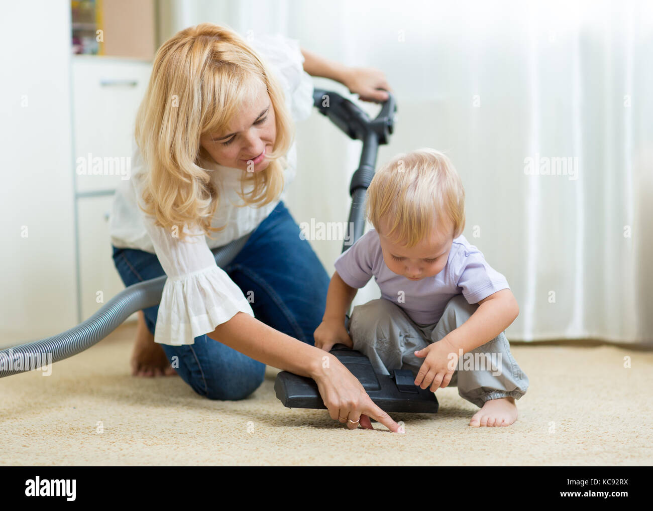 La famiglia la madre e il bambino ragazzo la pulizia della camera con aspirapolvere - lavori di casa Foto Stock