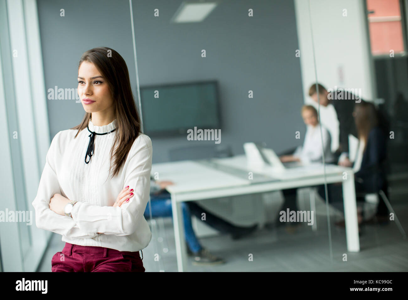 Giovane imprenditrice in piedi in un ufficio moderno con giovani uomini di affari in background che stringono le mani Foto Stock