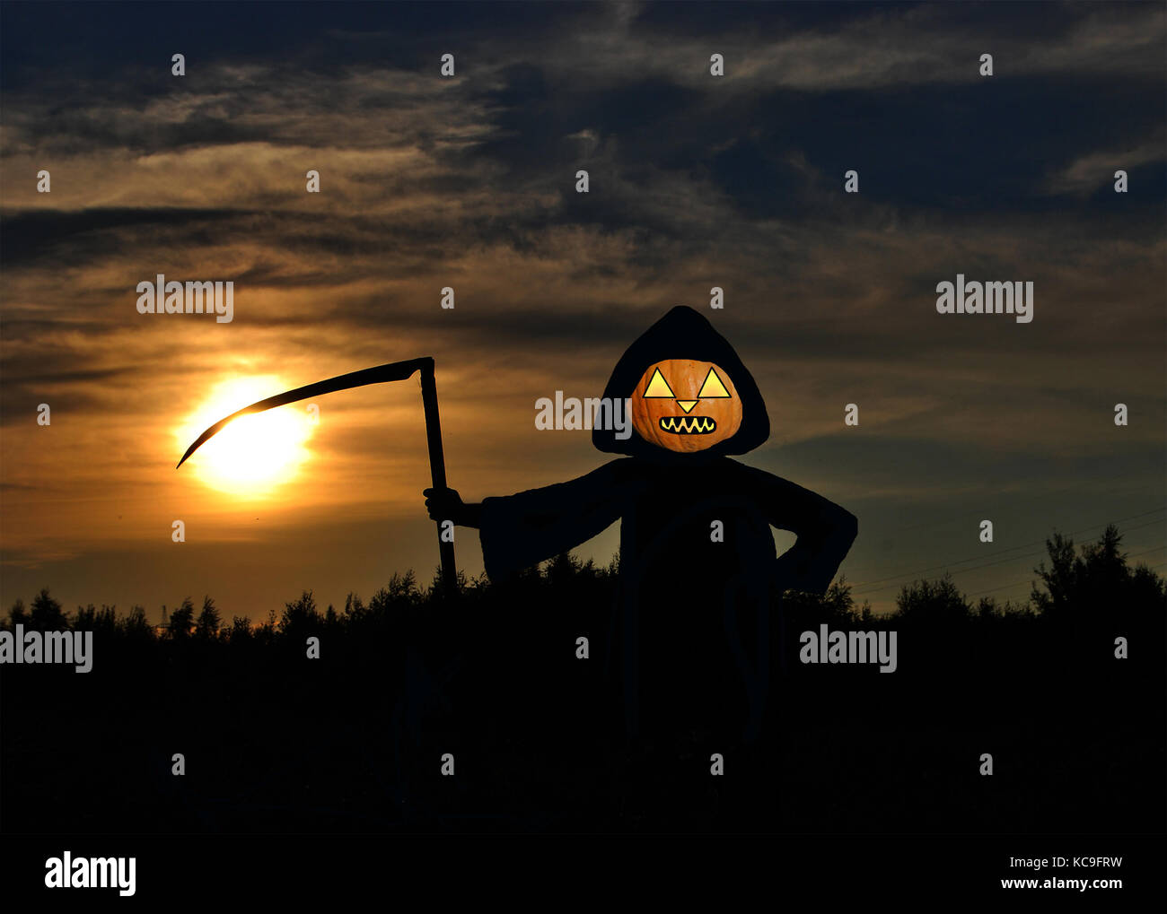 Jack-o-lantern in un mantello nero e con un ferro da stiro a falce contro il sole di setting Foto Stock