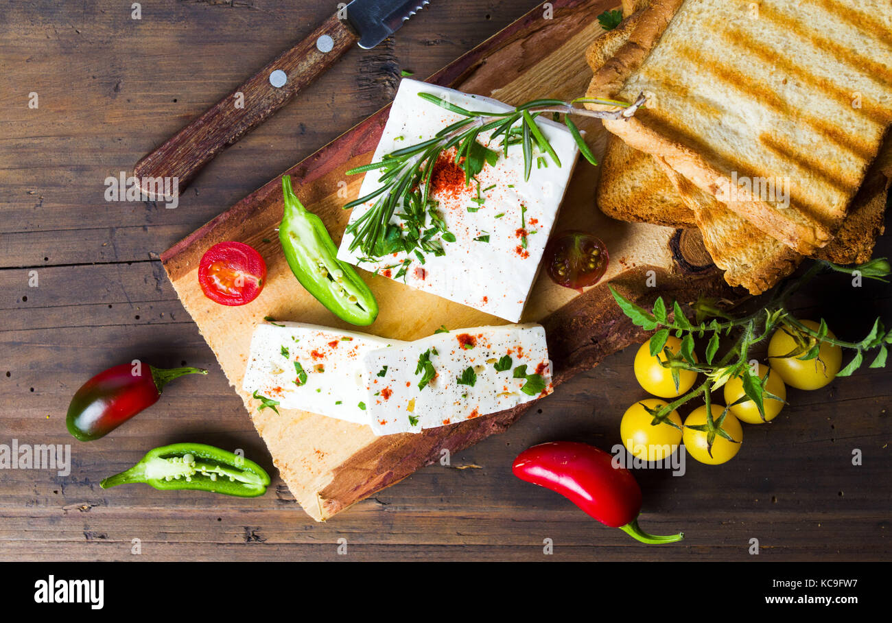 Formaggio con verdura e pane tostato naturale sul pannello di legno Foto Stock