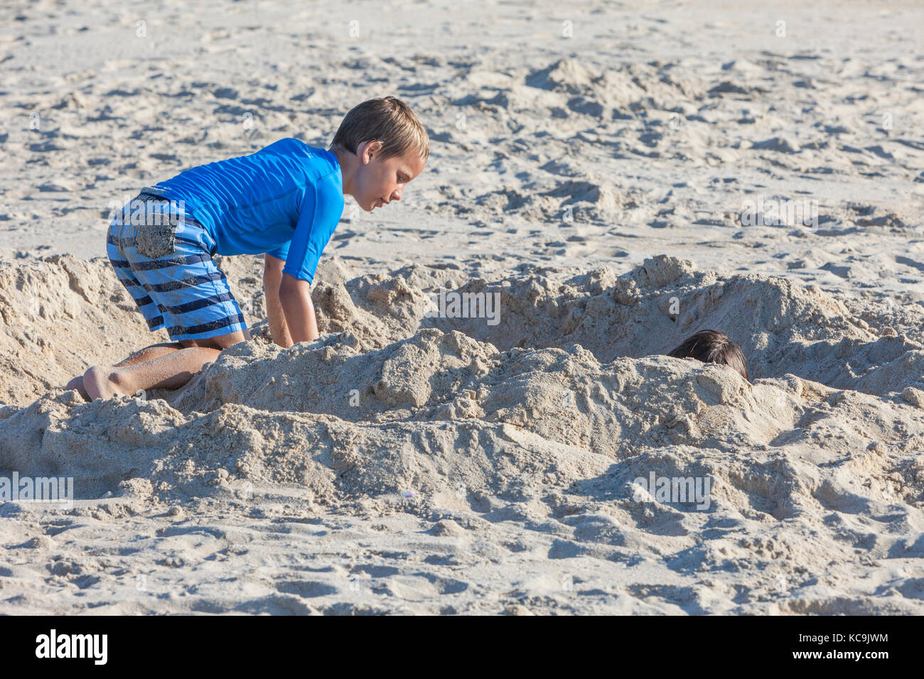 Avon, Outer Banks, North Carolina, Stati Uniti d'America. Giovane ragazzo il controllo sul suo fratello, sepolto nella sabbia. Foto Stock