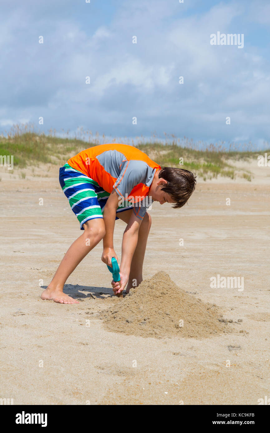 Avon, Outer Banks, North Carolina, Stati Uniti d'America. Ragazzo di scavare nella sabbia sulla spiaggia. Foto Stock