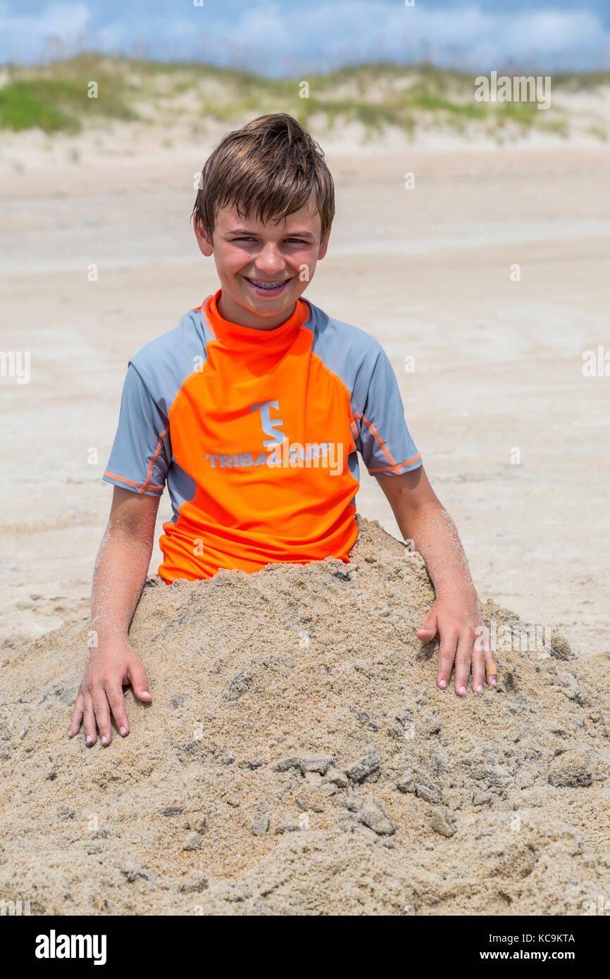 Avon, Outer Banks, North Carolina, Stati Uniti d'America. Ragazzo giovane sepolto nella sabbia. Foto Stock