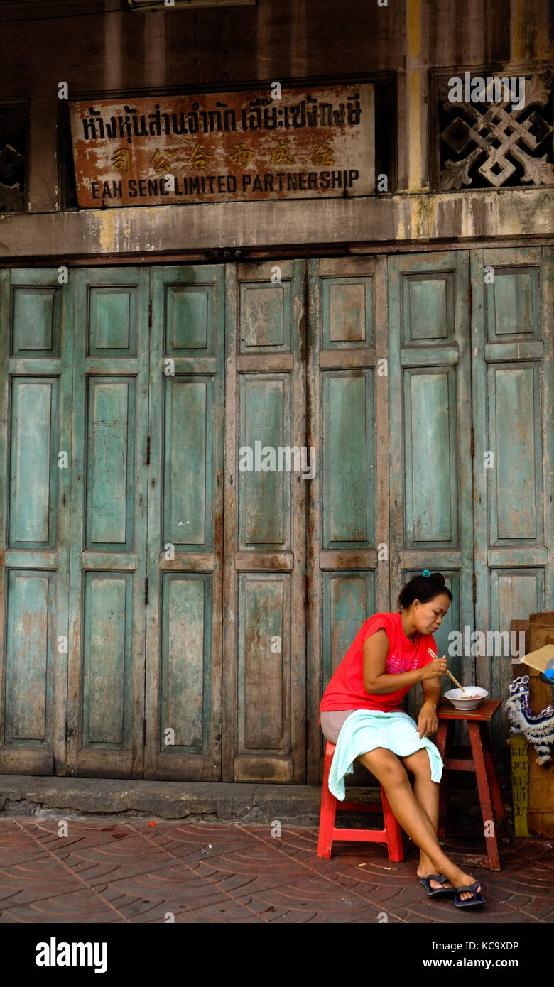 Una donna tailandese mangia cibo di strada fuori da un vecchio edificio a Chinatown, Bangkok Foto Stock