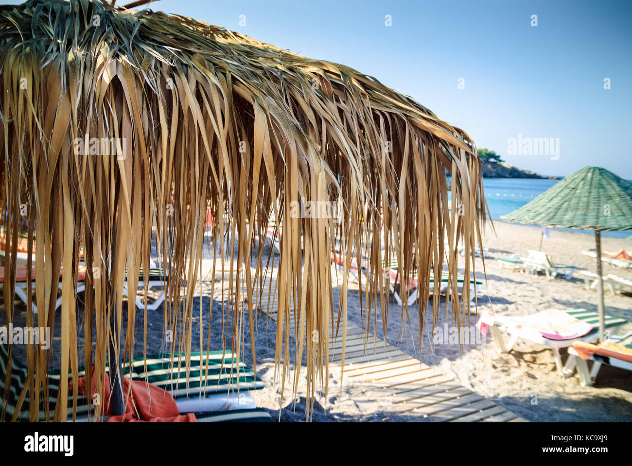 Scena di spiaggia con ombrellone di foglie di palma in primo piano Foto Stock