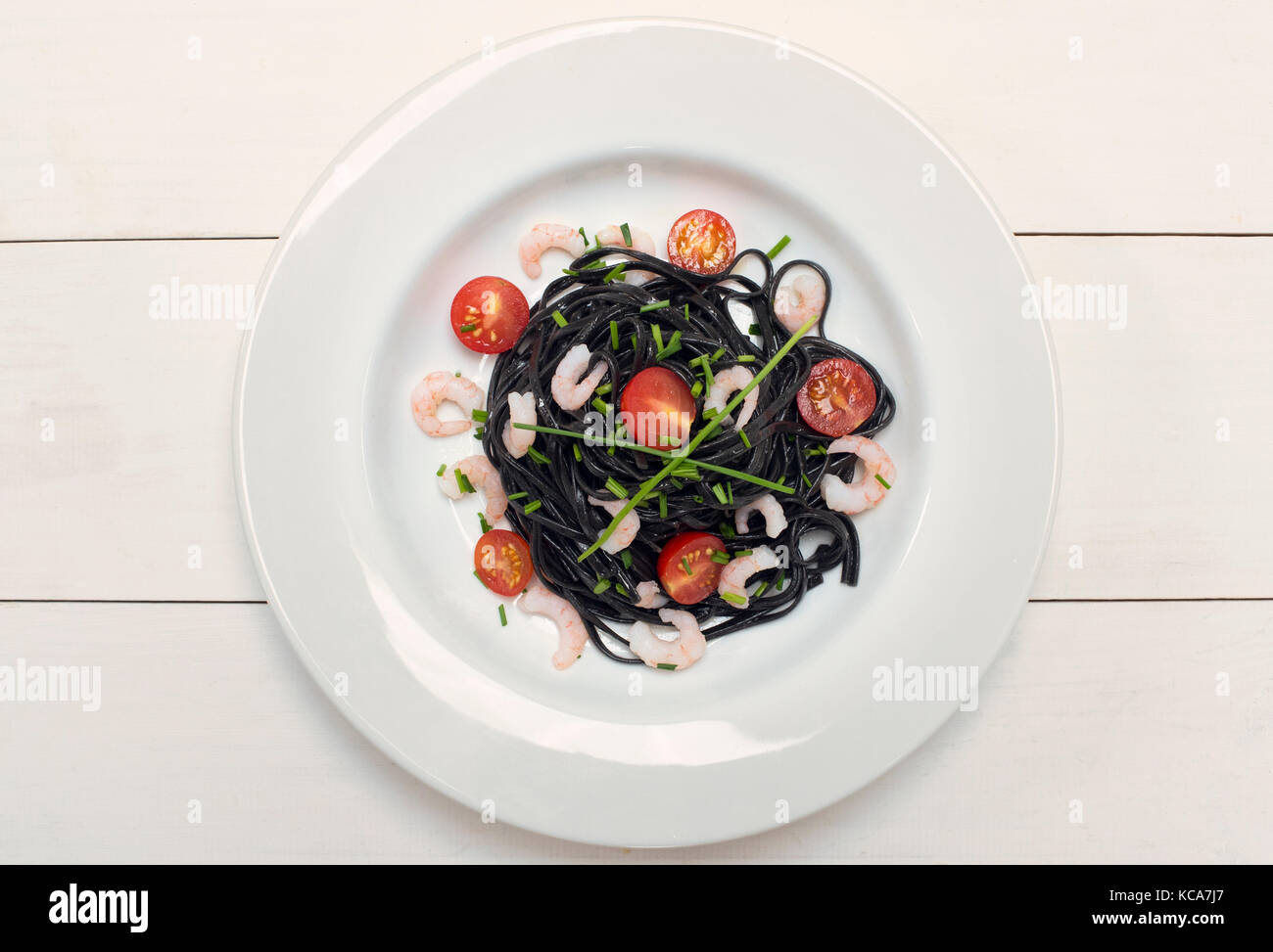 Calamari inchiostro nero pasta con gamberetti, erba cipollina e pomodori su sfondo bianco Foto Stock