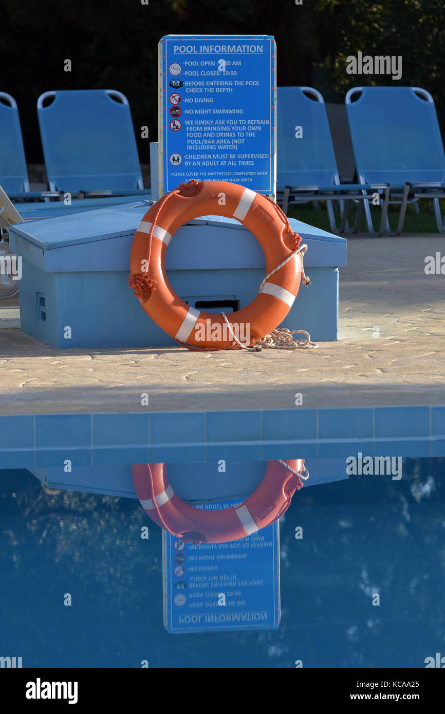 Un anello di vita o vita flottante aiuti di salvataggio sul lato di un vuoto piscina presso un hotel di Corfù, Grecia. sedie a sdraio e lettini accanto ad una piscina. Foto Stock