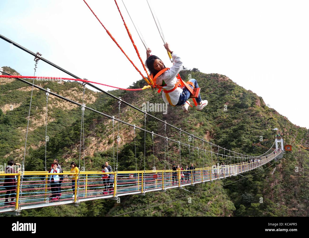 Shijiazhuang, la provincia cinese di Hebei. 4 ottobre 2017. Un turista gioca sull'altalena vicino al ponte con fondo in vetro durante le vacanze per la giornata Nazionale e il Festival di metà autunno in una valle nella città di Qian'an, nella provincia di Hebei della Cina settentrionale, 4 ottobre 2017. Il Festival di metà autunno di quest'anno si terrà il 4 ottobre. Il Festival di metà autunno, il 15° giorno dell'ottavo mese del calendario lunare cinese, è un'occasione per riunioni di famiglia e noto come il momento per mangiare torte di luna. Crediti: Yang Shirao/Xinhua/Alamy Live News Foto Stock