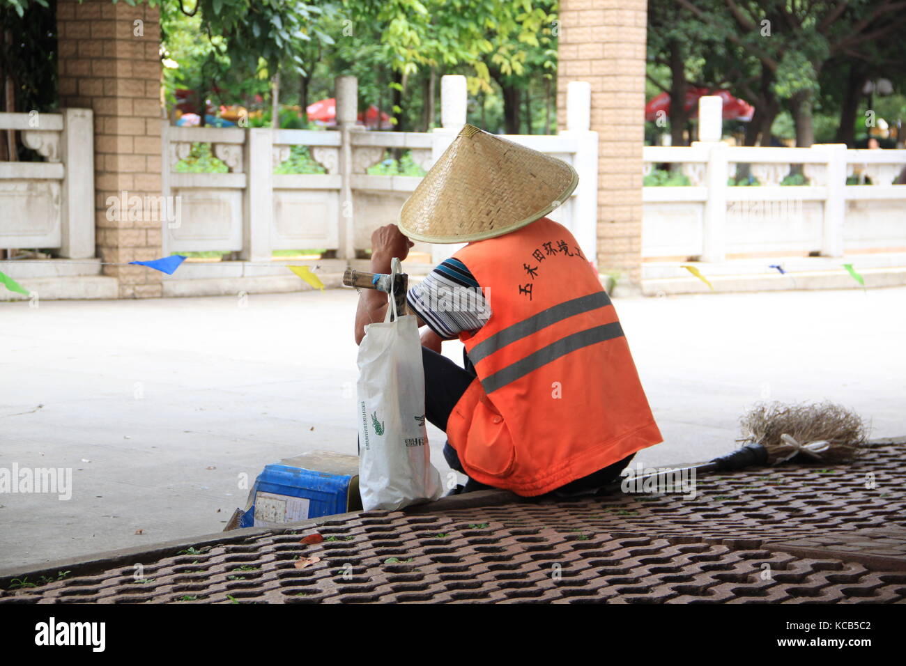 Lavoratore con riso hat seduto su un marciapiede Foto Stock