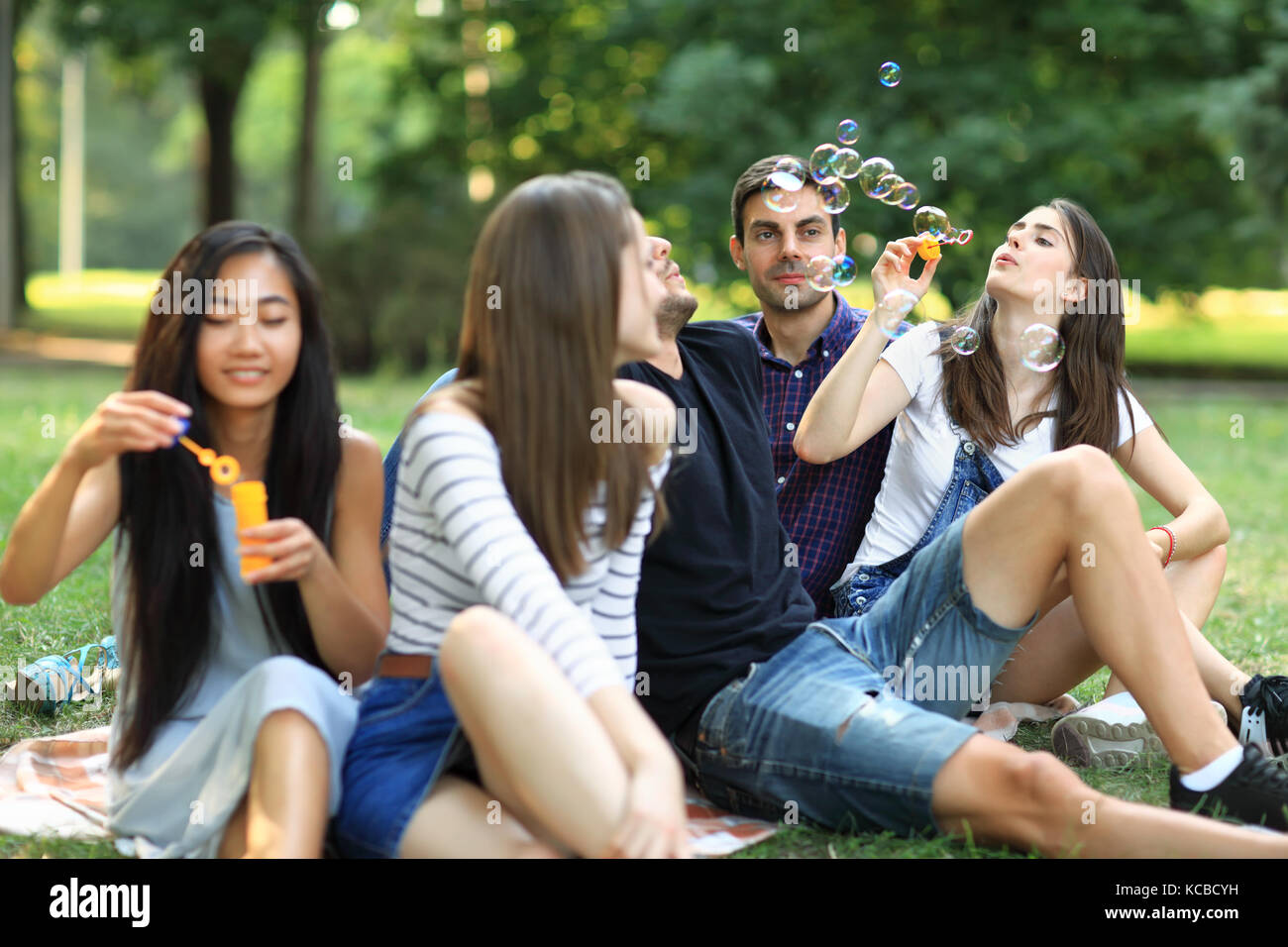 I migliori amici di riposo in park e soffiare bolle di sapone. giovani carefree gente seduta su erba e godere di ogni società di altri Foto Stock