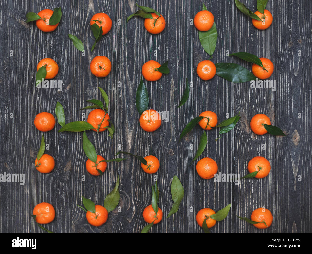 Il nuovo raccolto di mandarini giacente in una fila su legno scuro dello sfondo tessiturali Foto Stock