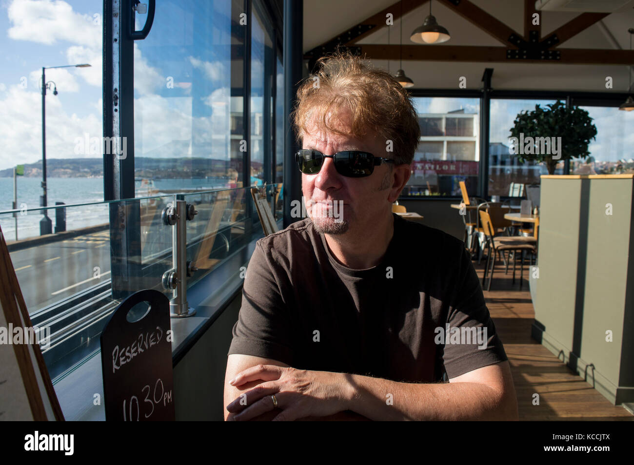 Felice l'uomo con pizzetto tenendo nella visualizzazione a coastal cafe in estate indossando occhiali da sole - foto Foto Stock