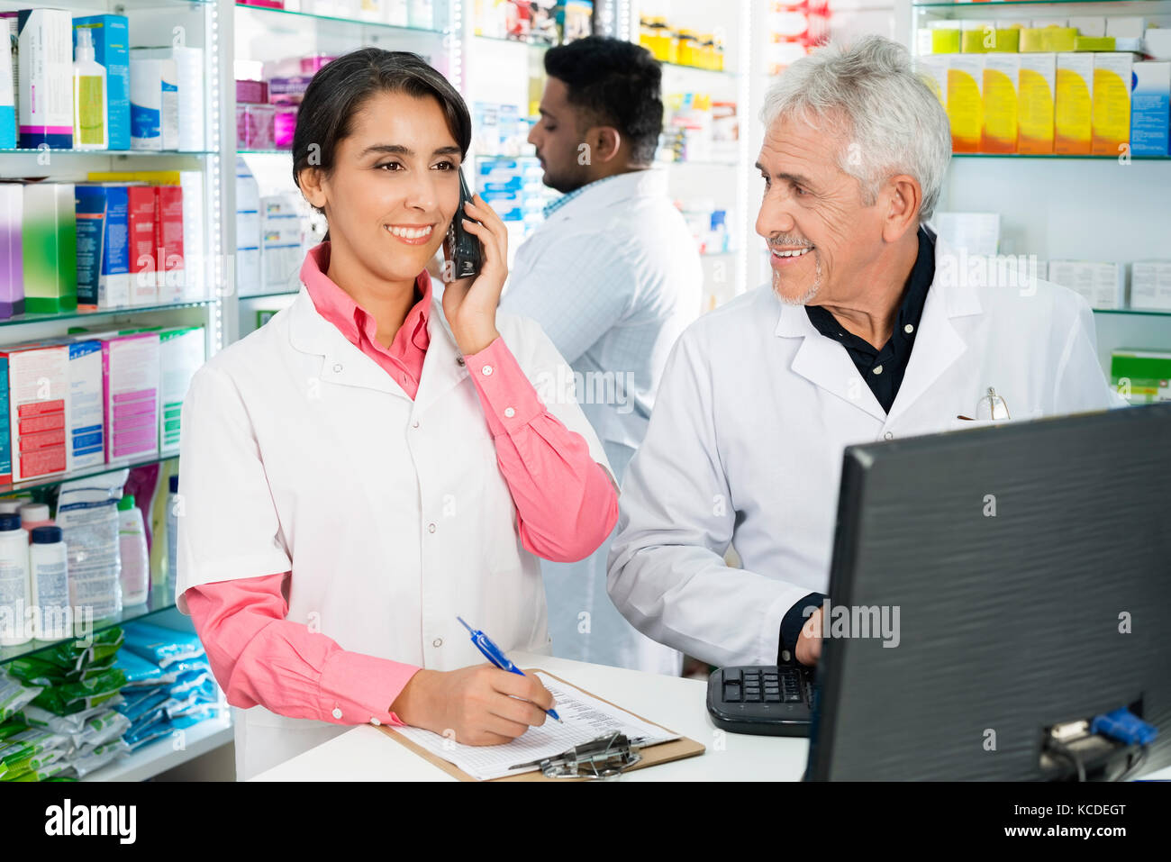 Sorridente chimico senior guardando collega tramite telefono al contatore in farmacia Foto Stock