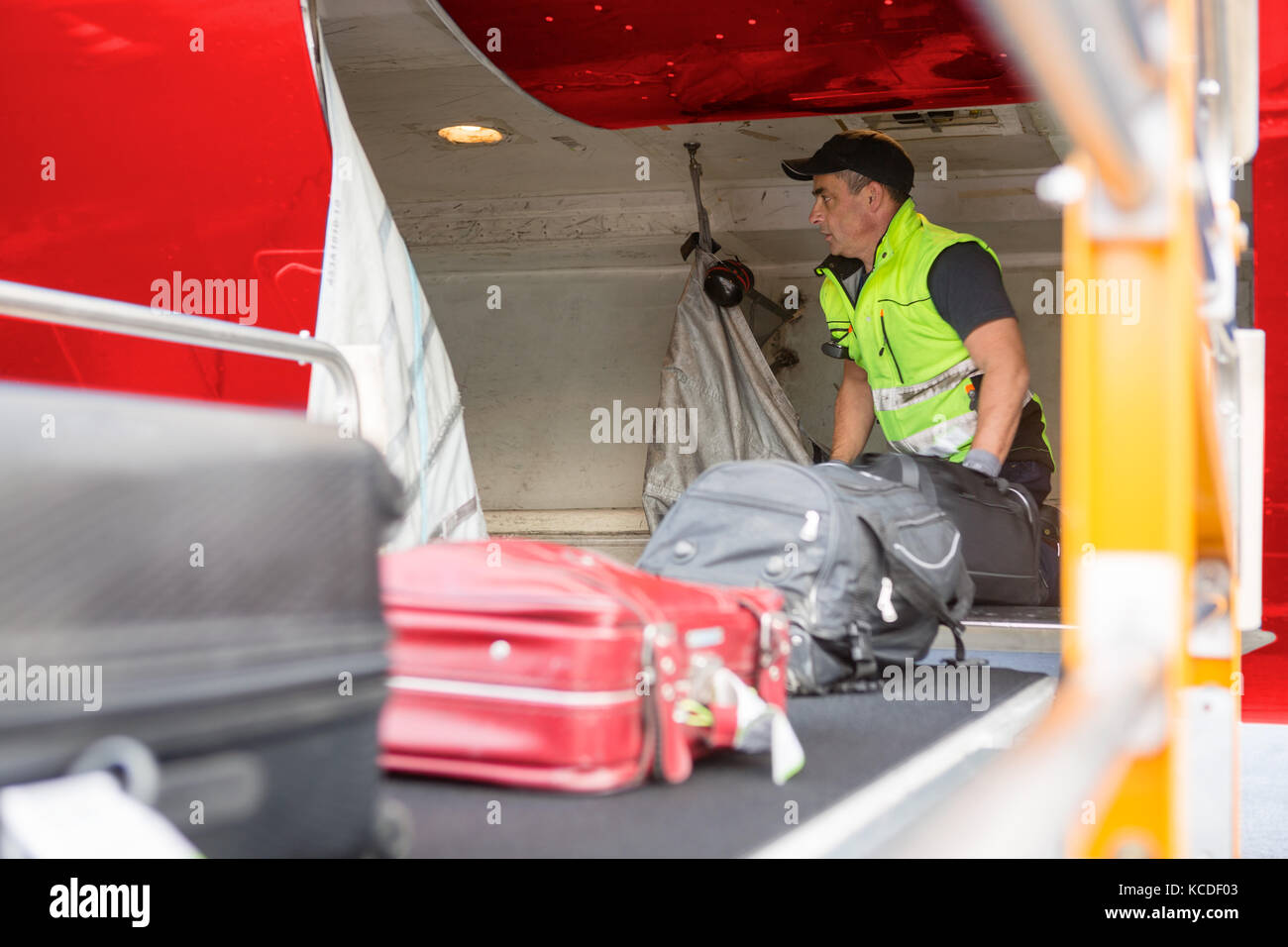 Maschio maturo lavoratore immissione di bagagli sul nastro di scarico aereo Foto Stock