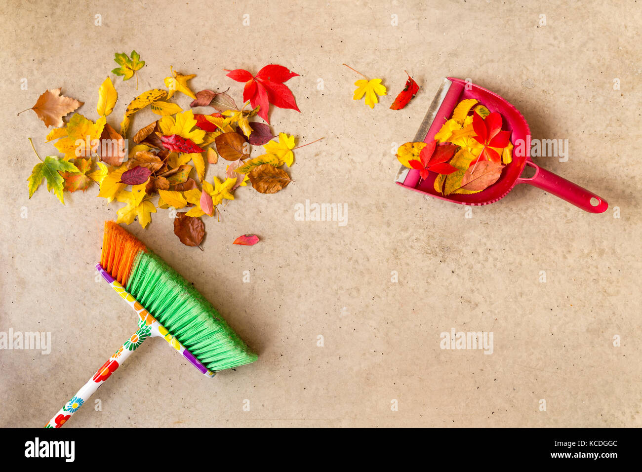 La pulizia a secco di foglie di autunno da un pavimento in cemento con una scopa colorato e pala Foto Stock
