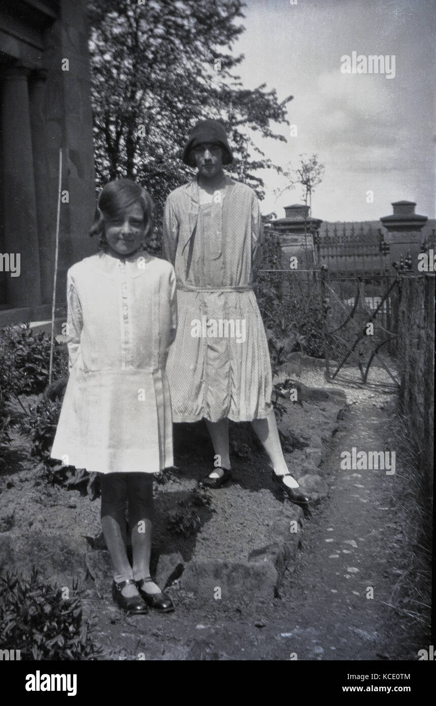 1920s, foto storiche che mostra una giovane donna e bambina in piedi al di fuori di una casa che indossa la moda femminile del giorno, Inghilterra, Regno Unito. Foto Stock