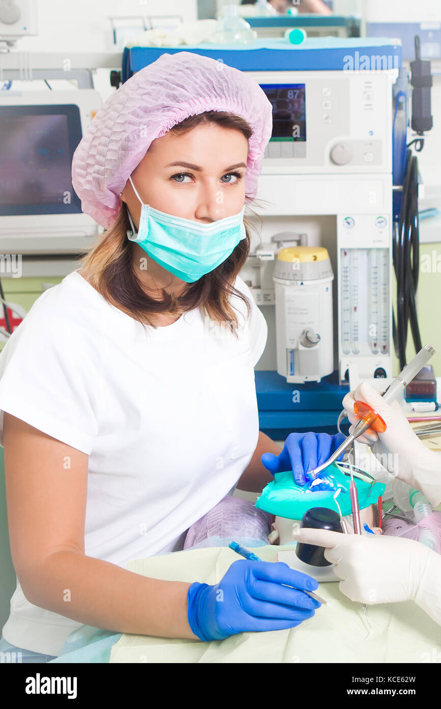 Una giovane donna dentista in bianco uniforme medica e un cappello rosa e  la sua assistente sorridente e facendo una procedura per il trattamento dei  denti da un bambino Foto stock -