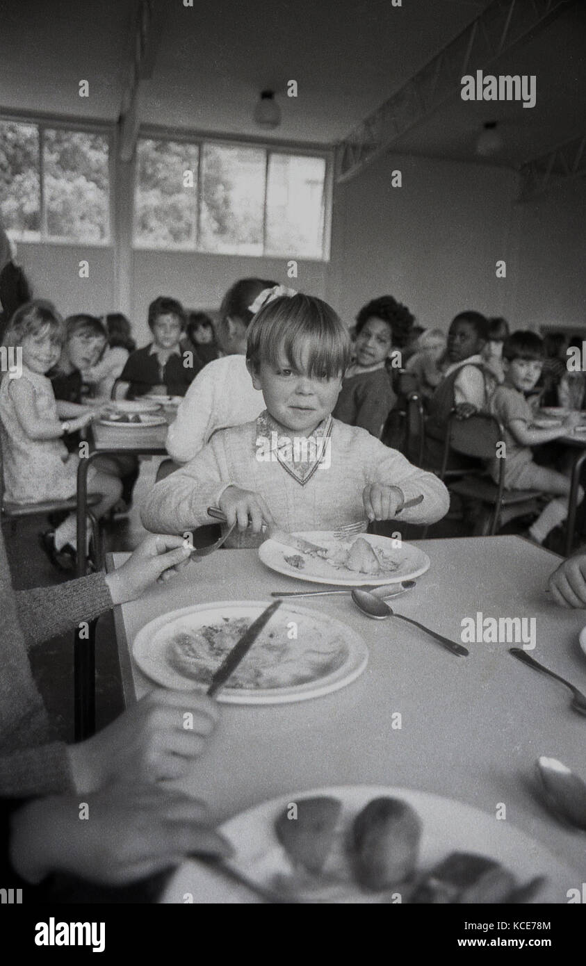 Anni Settanta, storico, immagine mostra un giovane ragazzo seduto a mangiare la sua scuola cena ad un tavolo con altri chldren Langbourne presso la scuola primaria. Dulwich, Londra, Inghilterra, Regno Unito. Foto Stock