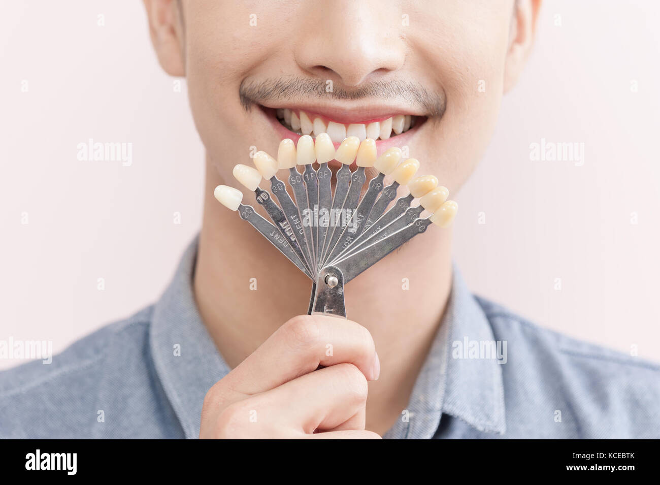 Maschio asiatici sorridere mentre il dente di trattenimento dei campioni di colore in mano. cure dentarie e concetto di manutenzione Foto Stock