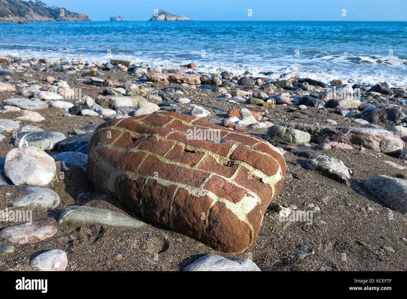 Piccola sezione di un muro di mattoni, mare-lavato ed eroso e lavato fino su Meadfoot Beach, Torquay, Devon, Regno Unito con la Thatcher rock in background. Foto Stock