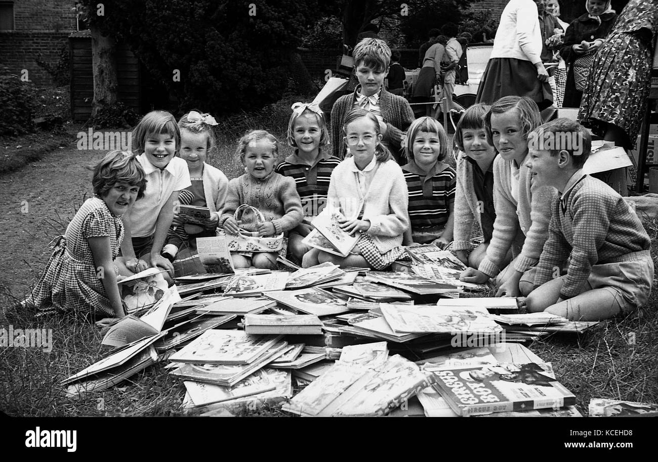 Anni sessanta, storico del gruppo di giovani bambini seduti insieme all'esterno con un gran mucchio di seconda mano libri a loro assegnato ad una carità fete Foto Stock