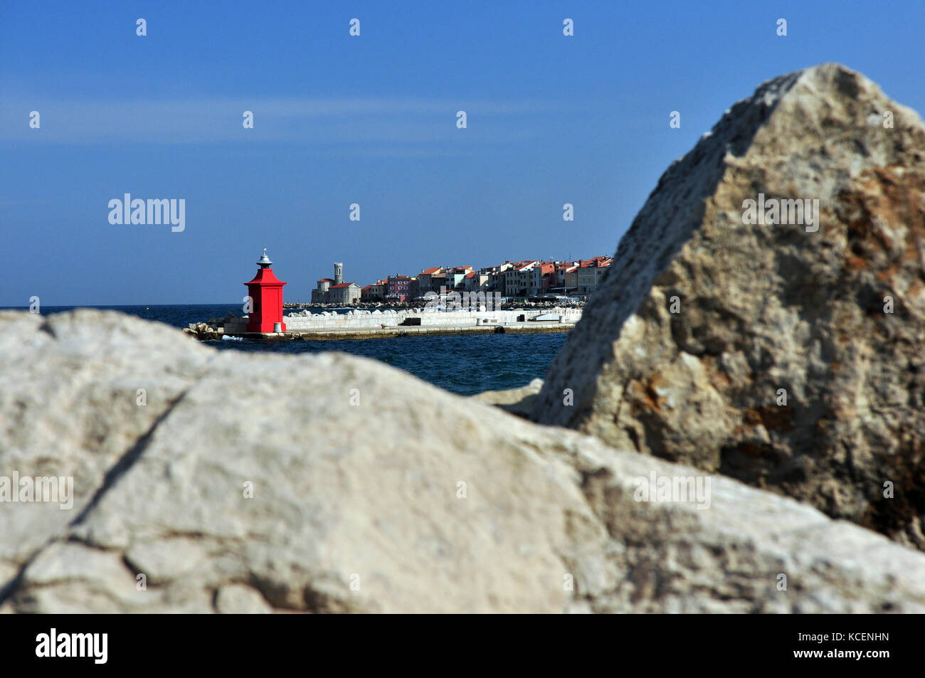 Faro rosso con la città di pirano in background con rocce in primo piano sullo sfondo di messa a fuoco Foto Stock