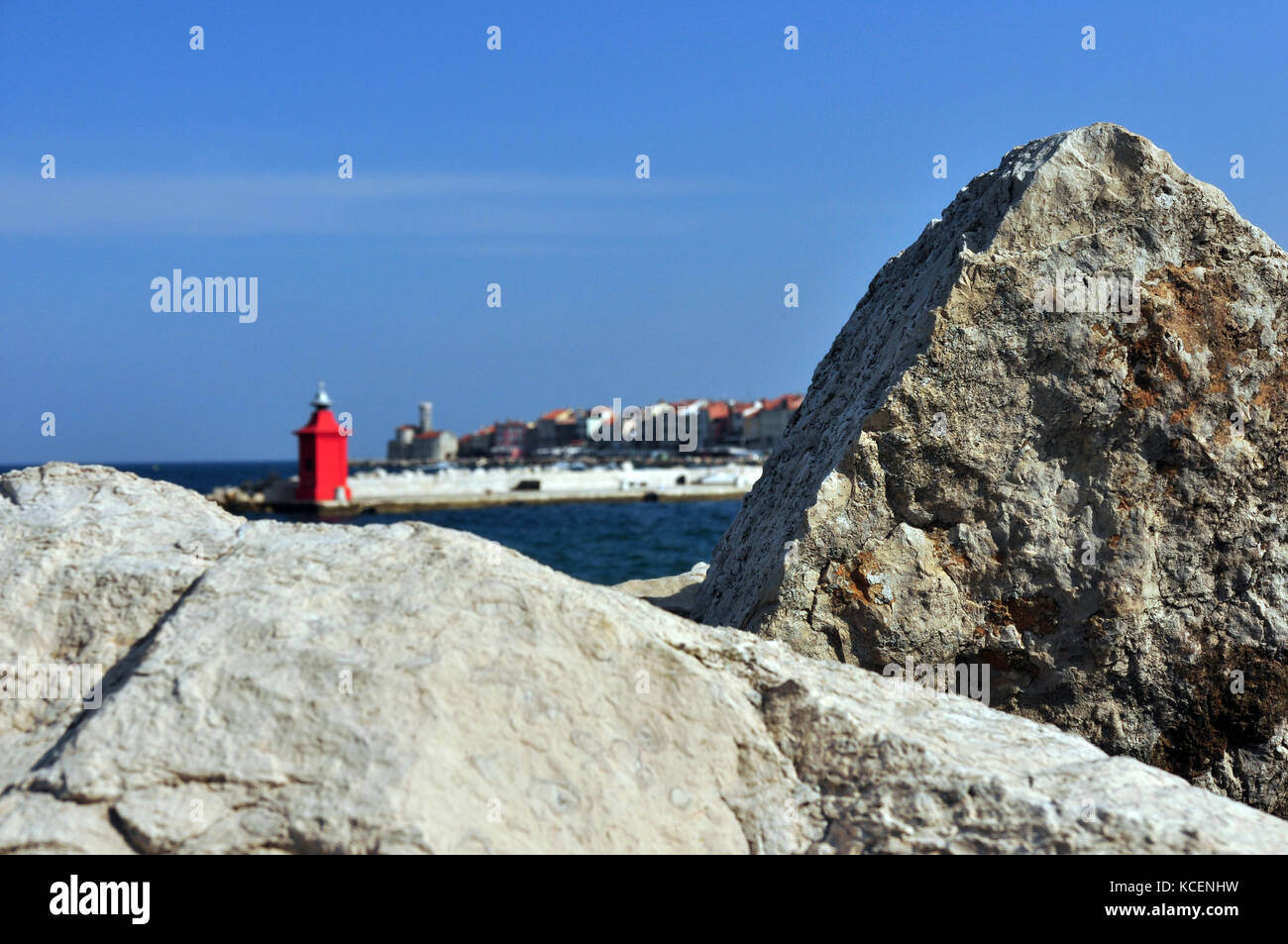 Faro rosso con la città di pirano in background con rocce in primo piano primo piano di messa a fuoco Foto Stock