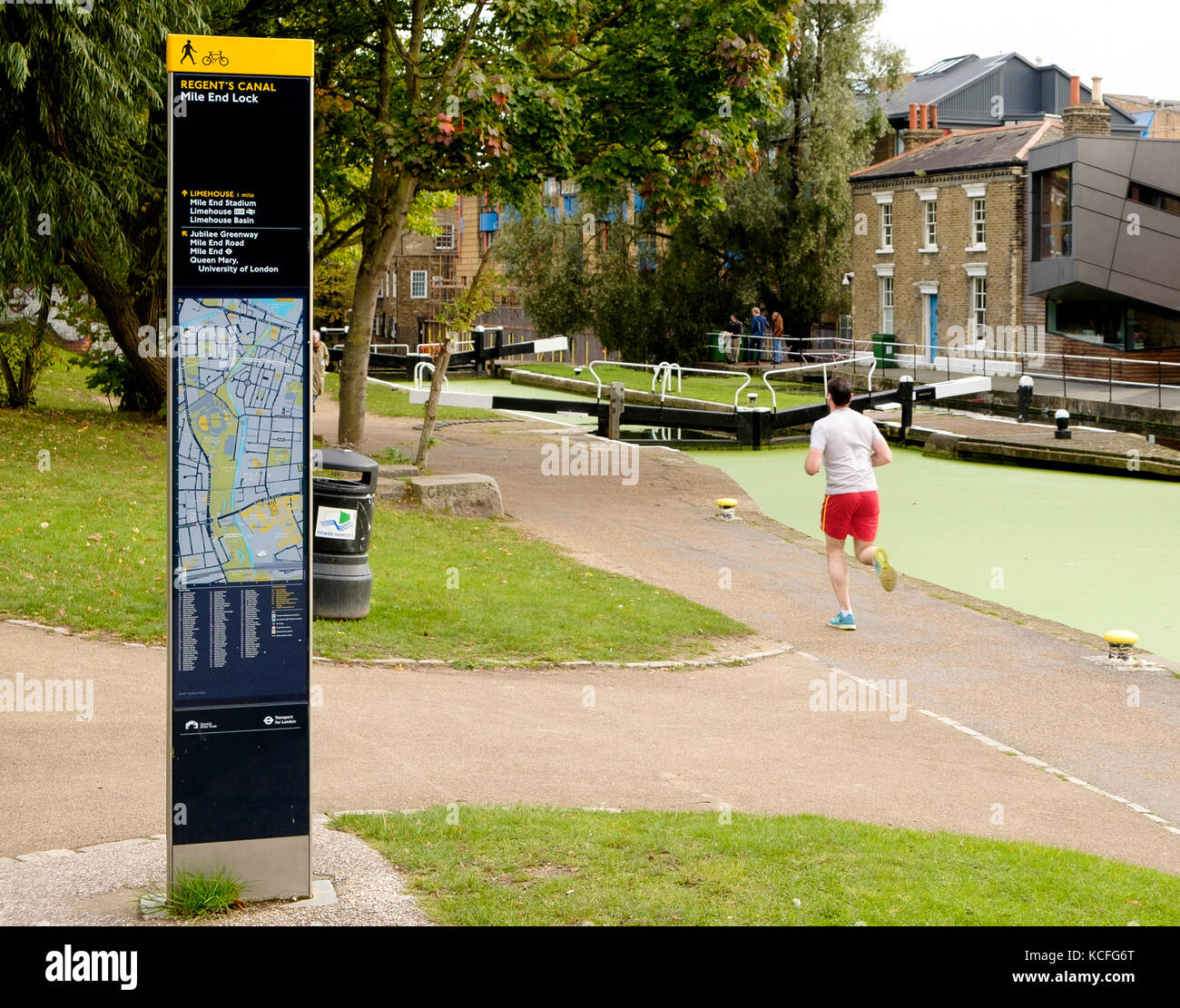 Un pareggiatore corre sul alzaia passando un cartello leggibile della London Column Street al Mile End Lock sul Regents Canal, Londra Foto Stock