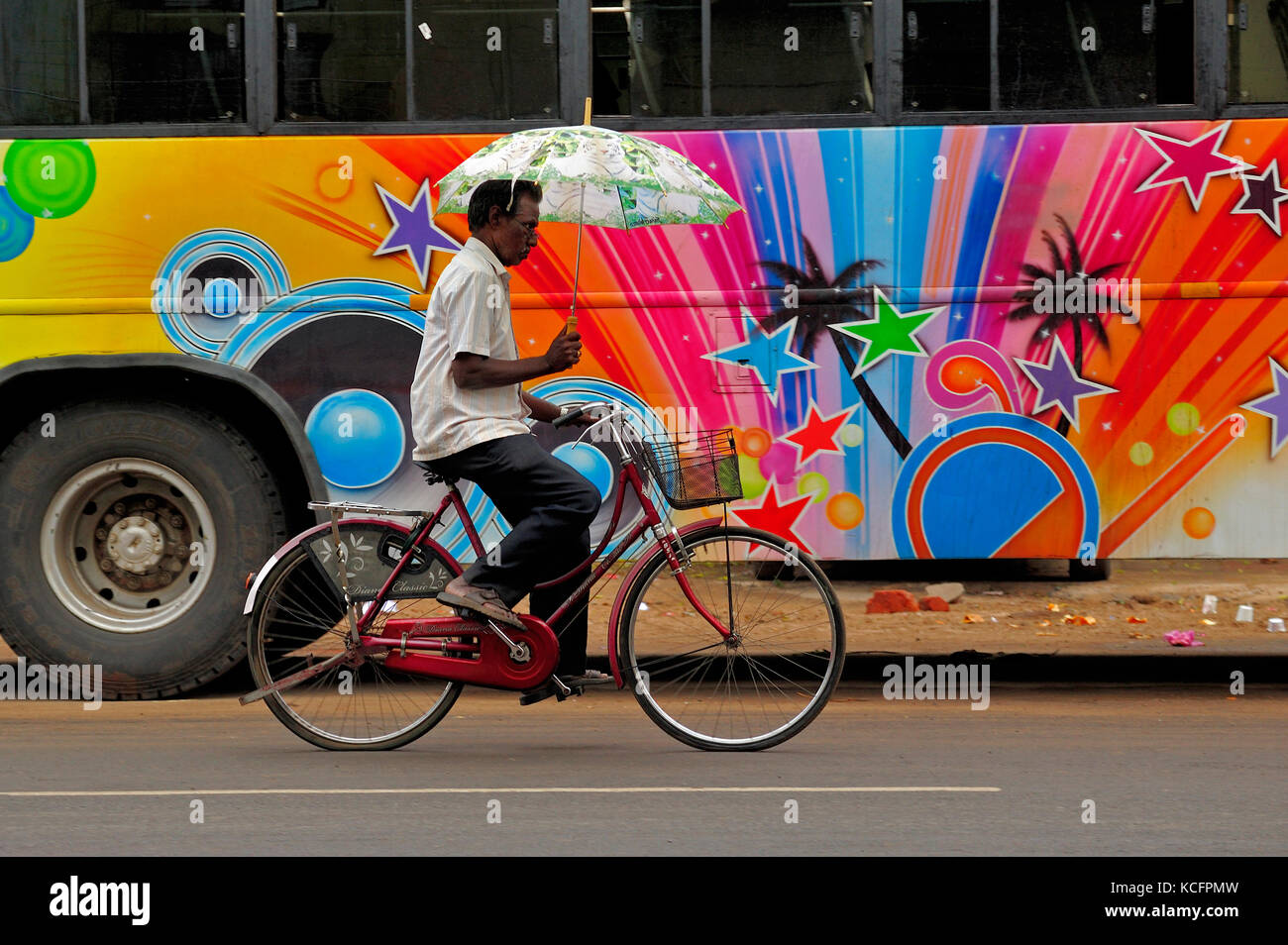 Uomo in bicicletta con un ombrello con autobus colorato, Chidambaram, Tamil Nadu, India Foto Stock