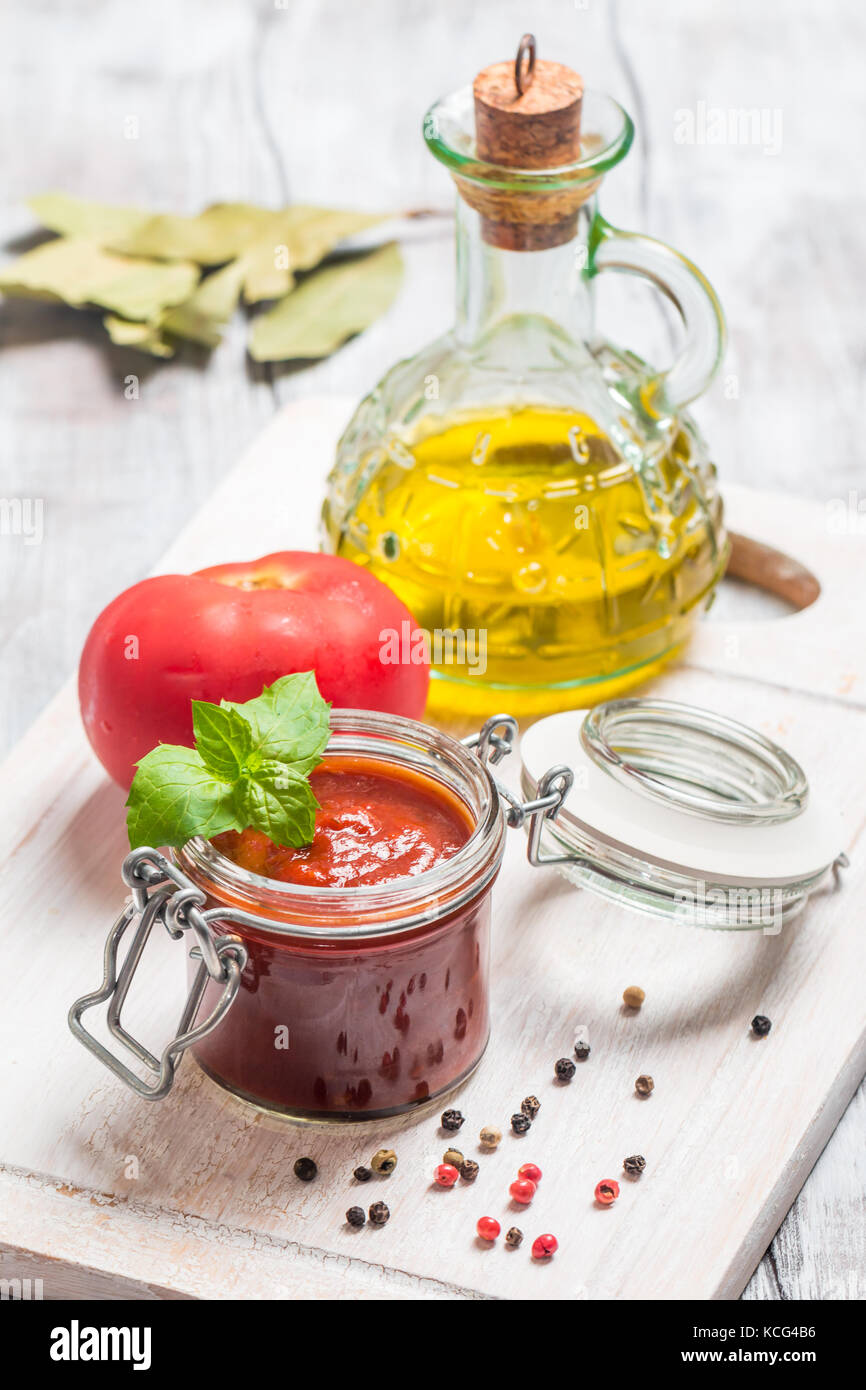 Il vasetto di vetro con fatti in casa classico pomodoro piccante pasta o pizza sauce. italiano cibo sano in bianco sullo sfondo di legno. Foto Stock