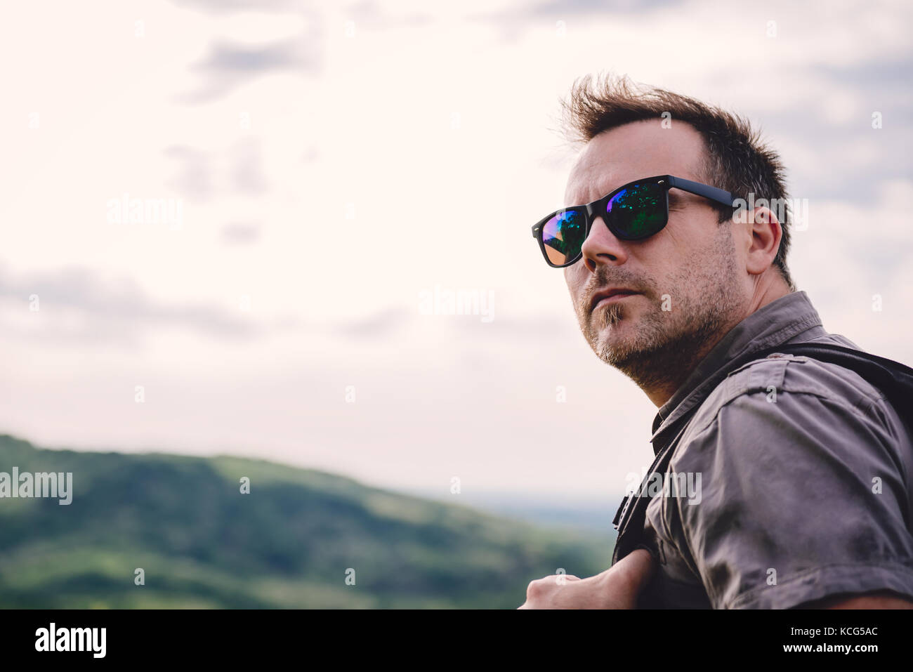 Uomo che indossa gli occhiali da sole e zainetto guardando indietro Foto Stock