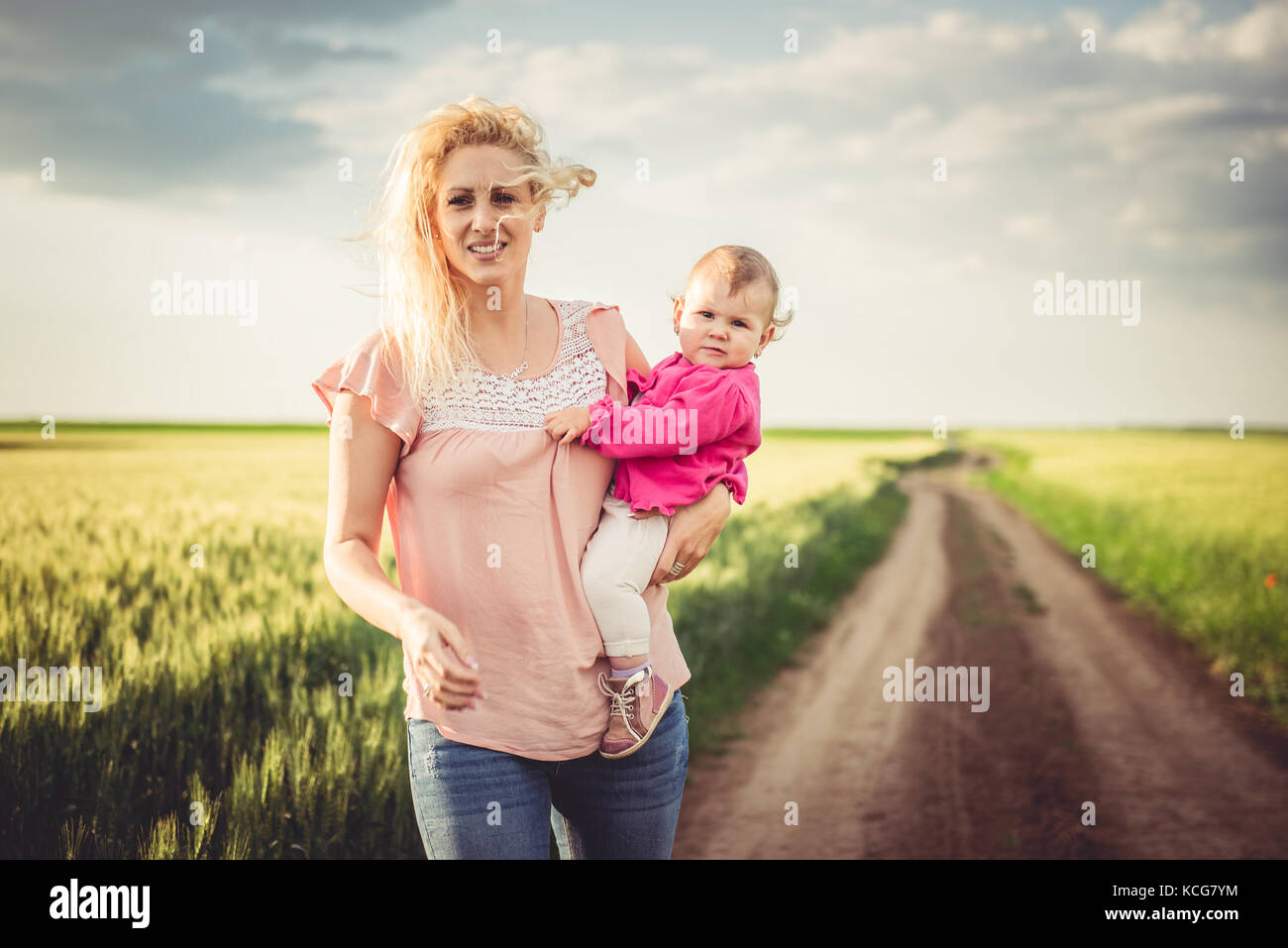 Madre tenendo la sua bambina tra le sue braccia e camminare sulla strada di ghiaia dai campi di grano Foto Stock