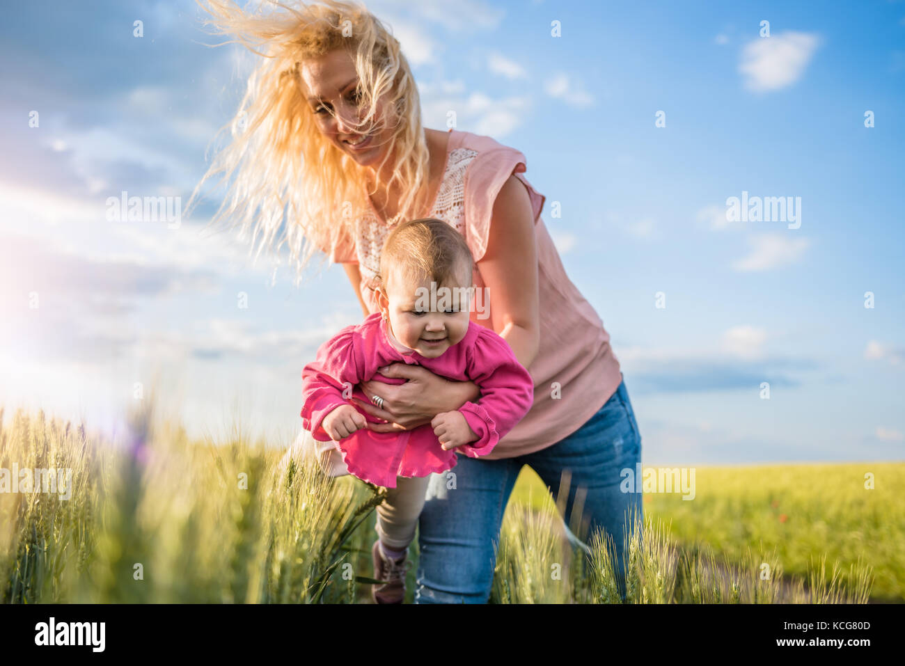 Felice madre tenendo la sua bambina le braccia nel campo di grano Foto Stock
