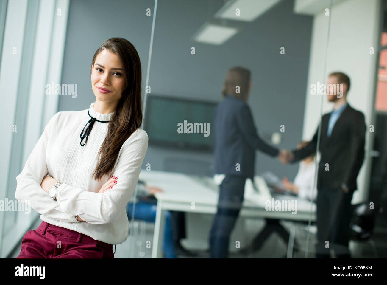 Giovane imprenditrice in piedi in un ufficio moderno con giovani uomini di affari in background che seduta Foto Stock