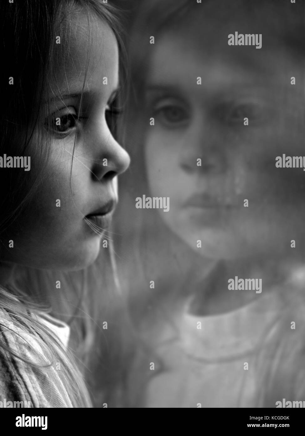 Piccola ragazza riflessa che guarda fuori dalla finestra. Foto Stock
