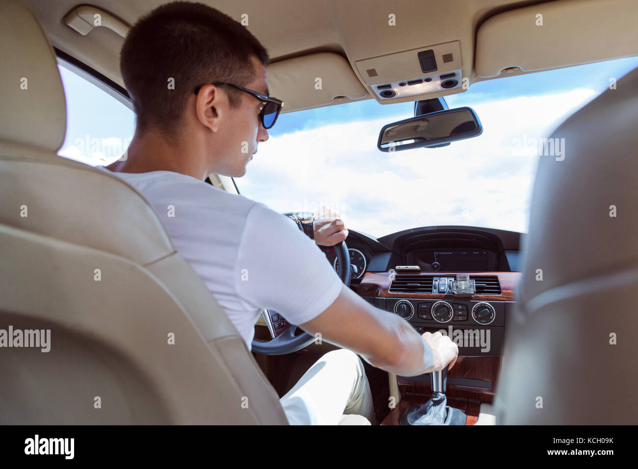 Giovane uomo elegante in occhiali da sole alla guida di un'auto. vista dal retro. Foto Stock