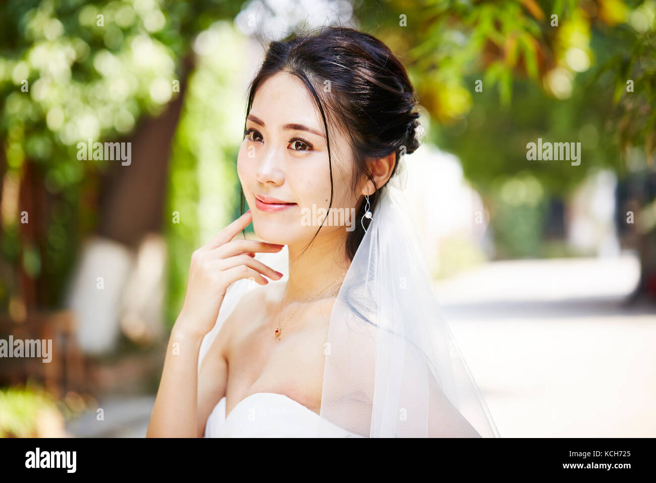 Outdoor ritratto della bella e felice di giovani asiatici sposa indossa velo nuziale. Foto Stock