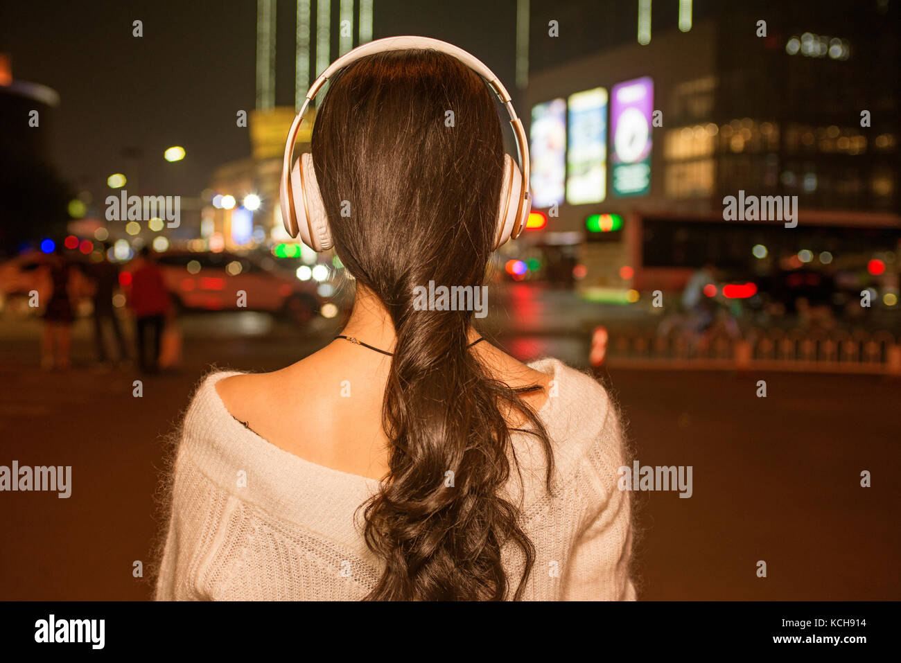 Ragazza per ascoltare musica con le cuffie sulle strade della città di notte Foto Stock