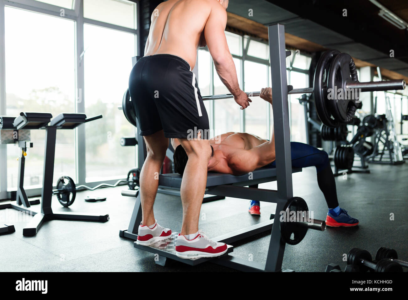Bel giovane uomo muscolare facendo la pressa da banco e ottiene aiuto Foto Stock